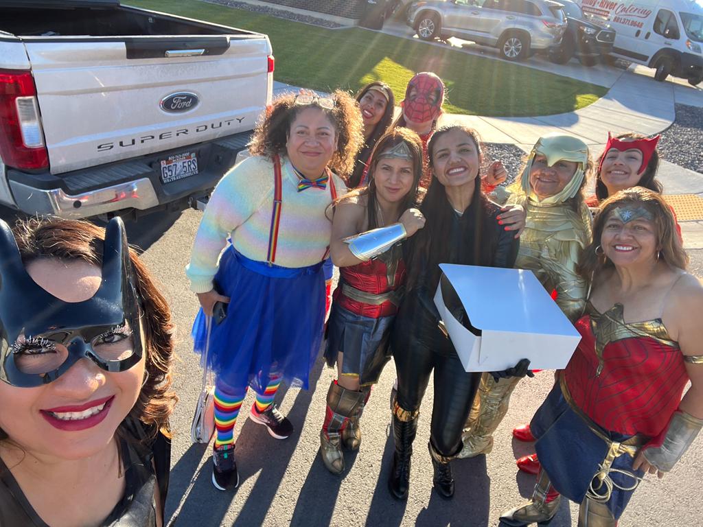 A group of people wearing colorful superhero costumes pose outdoors for a fun Halloween event.