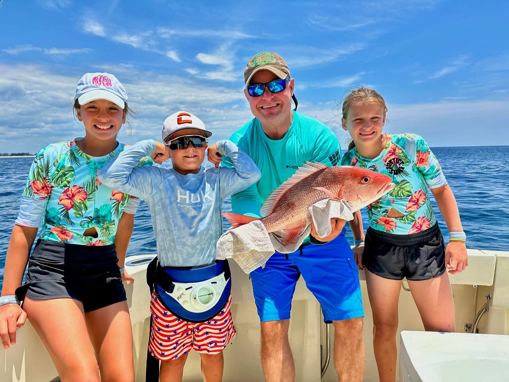 A happy family on a deep sea fishing charter holding a large red snapper caught in the ocean.
