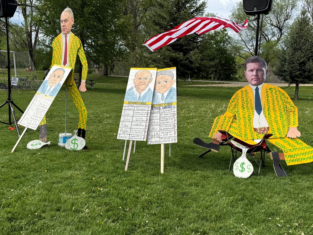 Political protest display featuring cardboard cutouts of candidates in dollar sign suits for a rally.