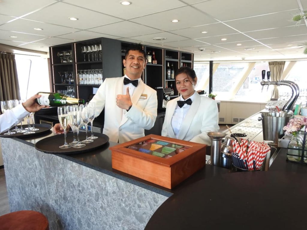 Waitstaff in white tuxedos pouring champagne at a luxury cruise ship bar.