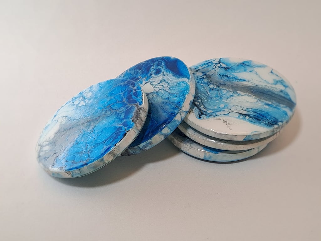 Handmade round coasters with blue and white fluid acrylic pour paint art in a marble design.