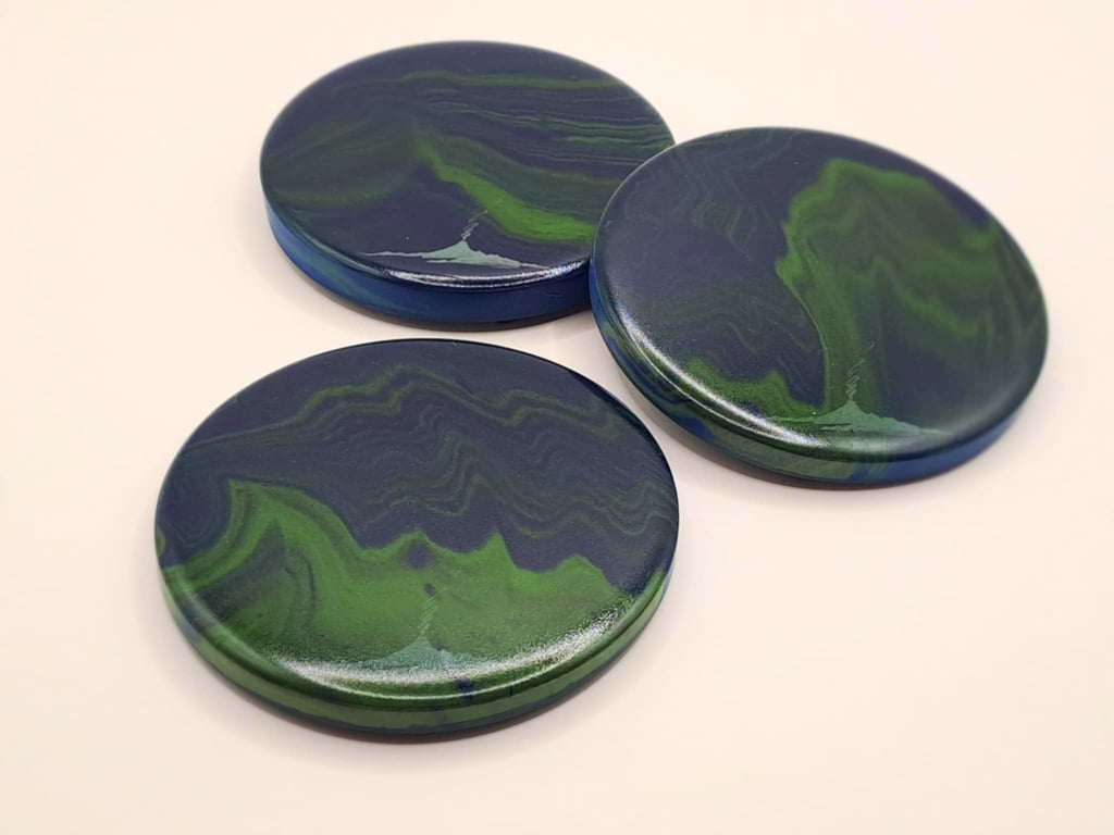 Three round handmade coasters with blue and green swirl patterns mimicking northern lights..