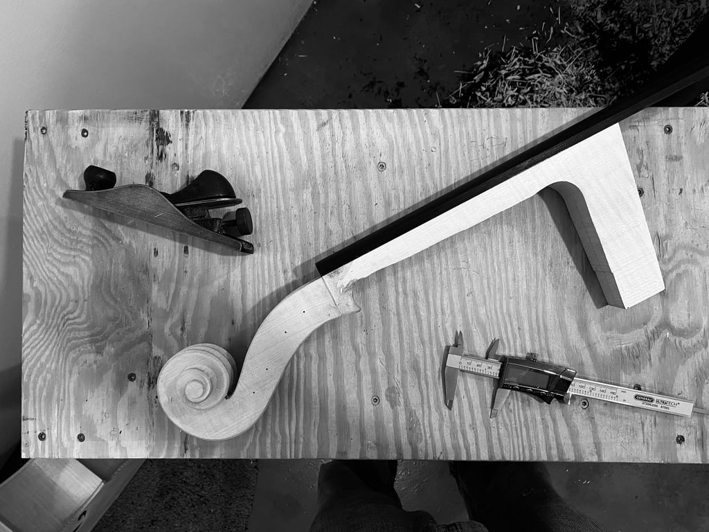 Flatlay pic of the cello neck, a plane, and caliper on the workbench before carving is complete.