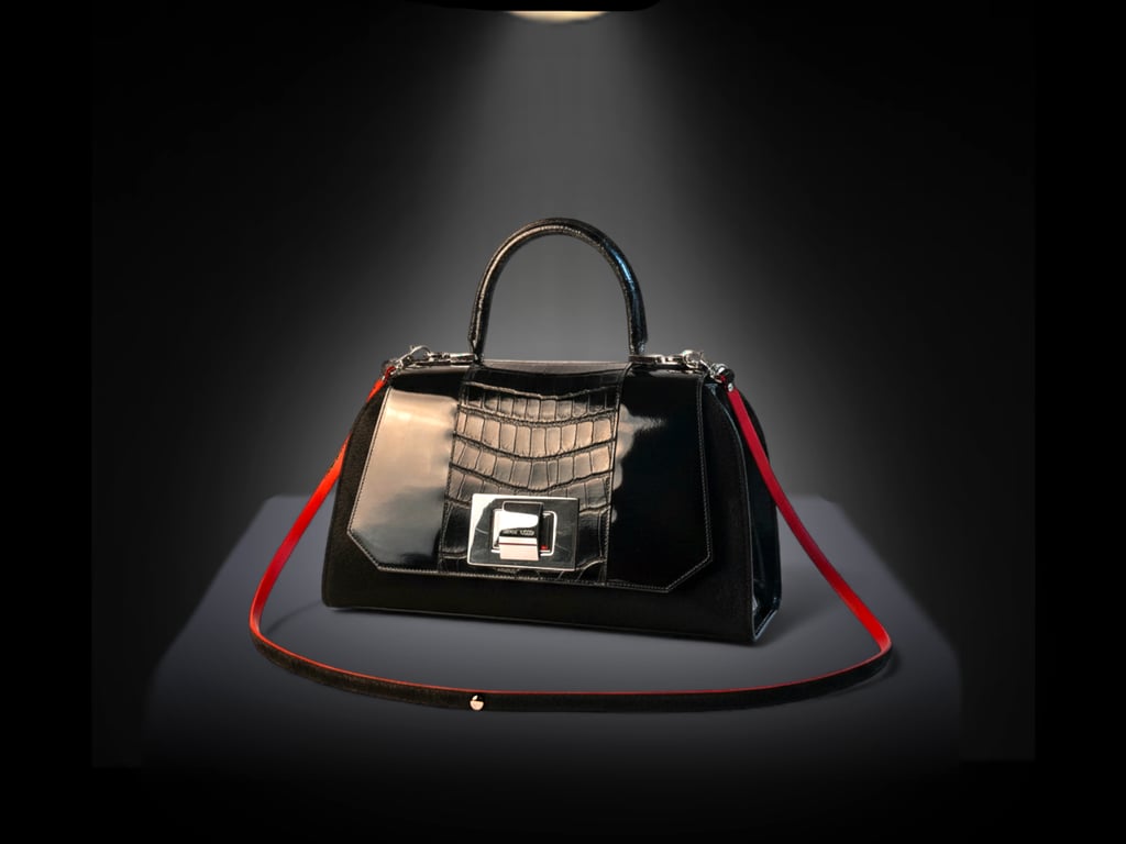 Elegant black leather handbag with crocodile texture and red strap under a spotlight.
