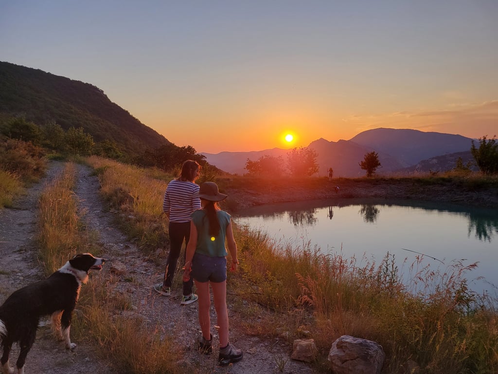people walking down a path and looking at the beatiful sunset above the mountains and a lake