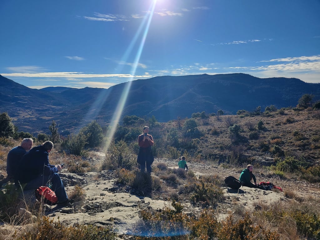 a group of people sitting and relaxing on a hill with a sun shining in the background