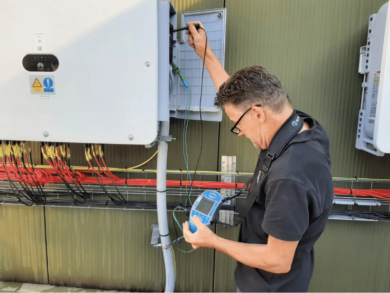 specteur voert metingen uit aan zonnestroominstallatie bij omvormer op buitenmuur