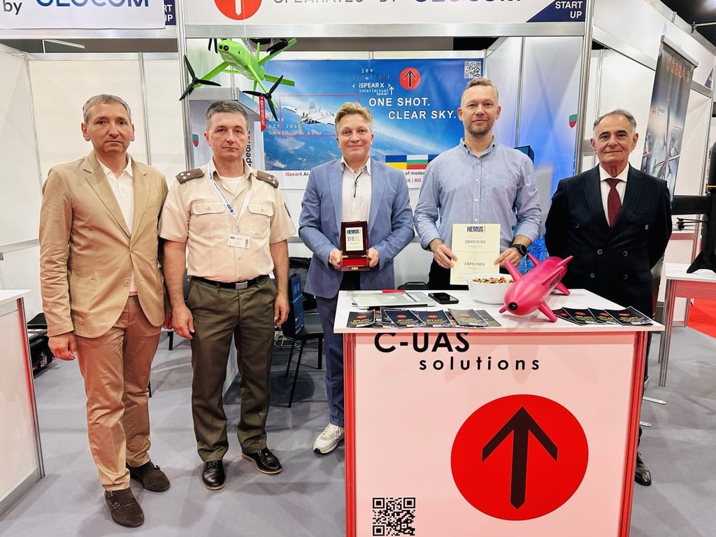 Five professionals presenting C-UAS drone solutions and award certificates at a technology defense exhibition booth.