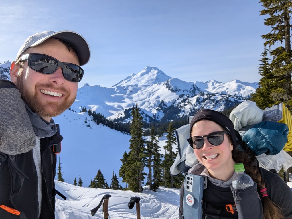 Moose and Bugs smiling in a selfie in front of snow-covered Mt. Baker on a beautiful winter day.
