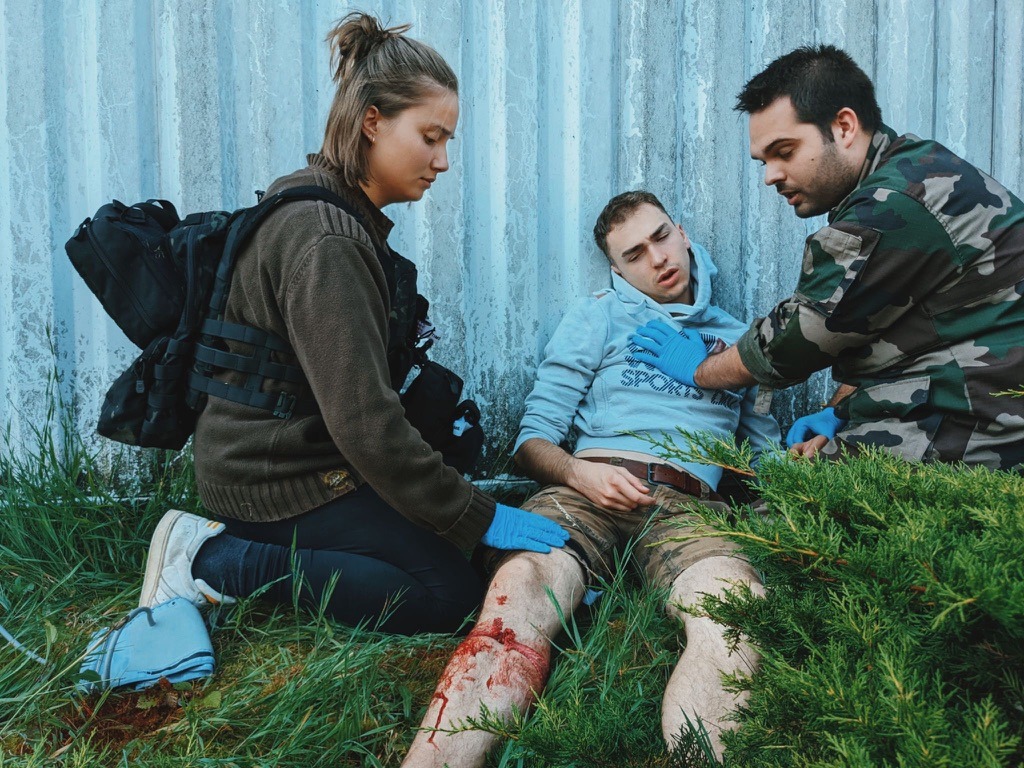 Emergency first responders providing tactical medical aid to an injured person with a leg wound.