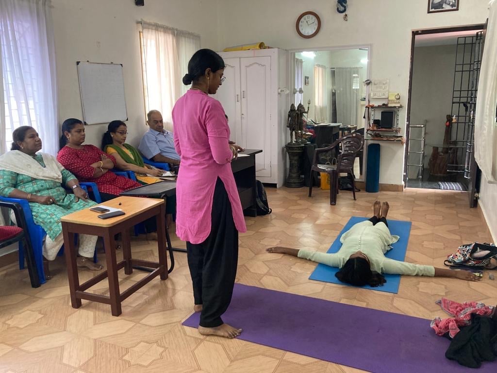 a woman in a pink shirt is standing in a room with several people during a teacher yoga class