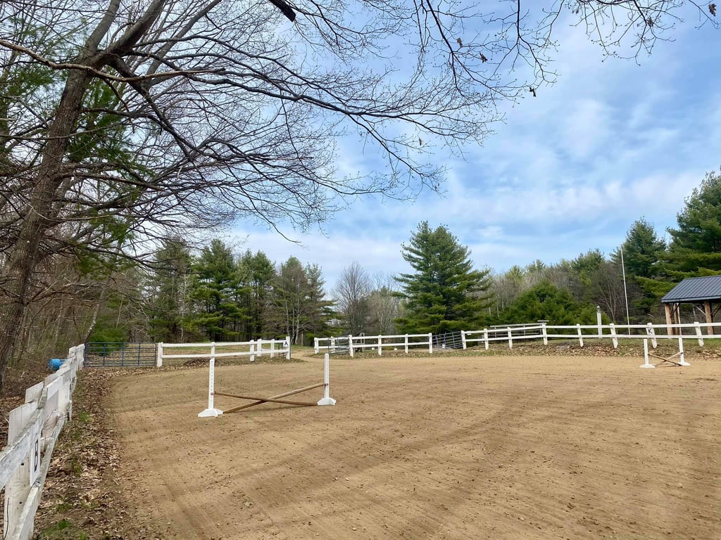 a horse riding arena with white fenced in area and trees