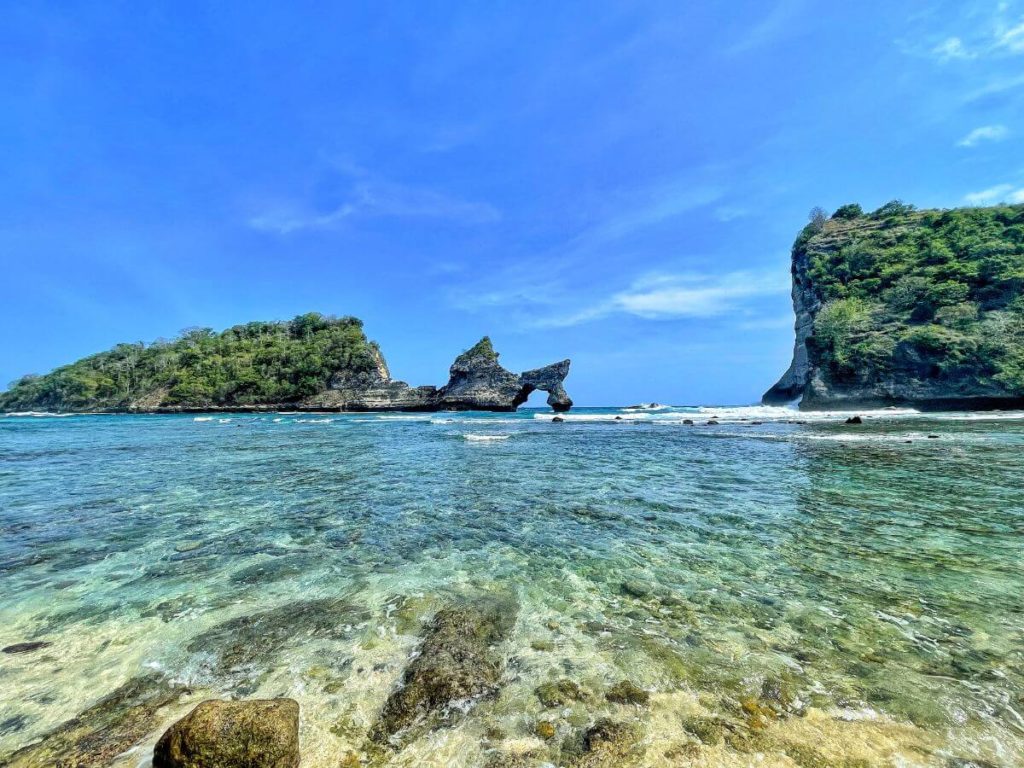 two women walking into turquoise ocean on a white sandy beach with limestone cliffs and lush green islands under blue sky