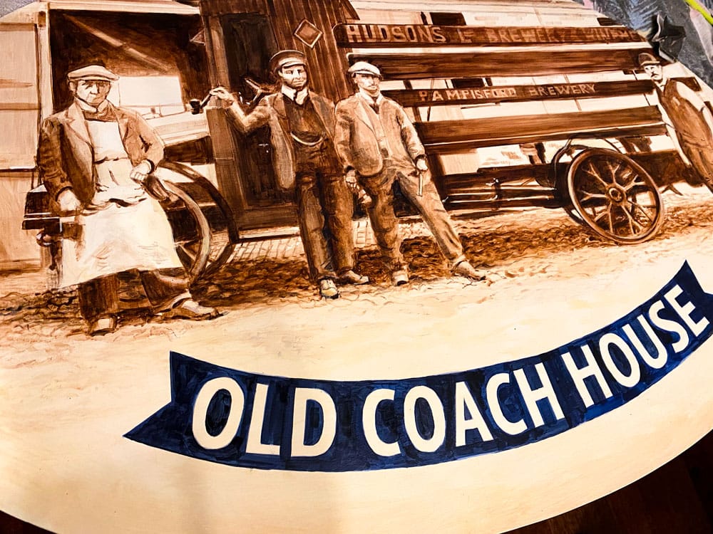 Close-up of angled pub sign with painted brewery staff