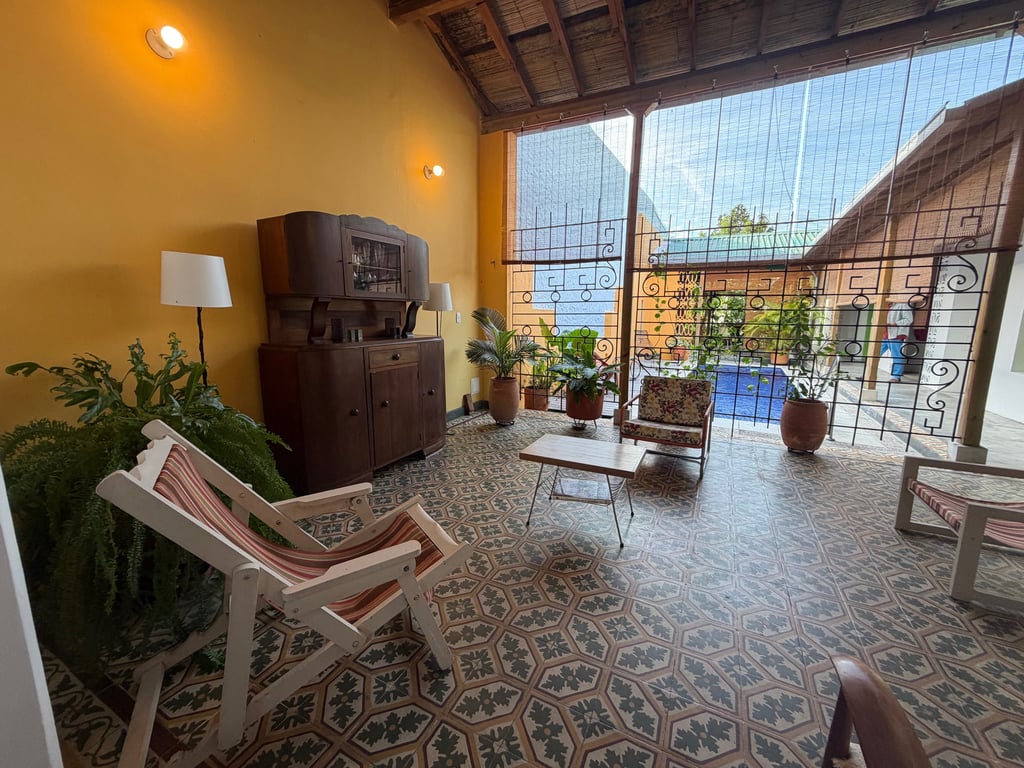 Rustic patio lounge with patterned floor tiles, antique wooden furniture, and a view of a garden swimming pool.