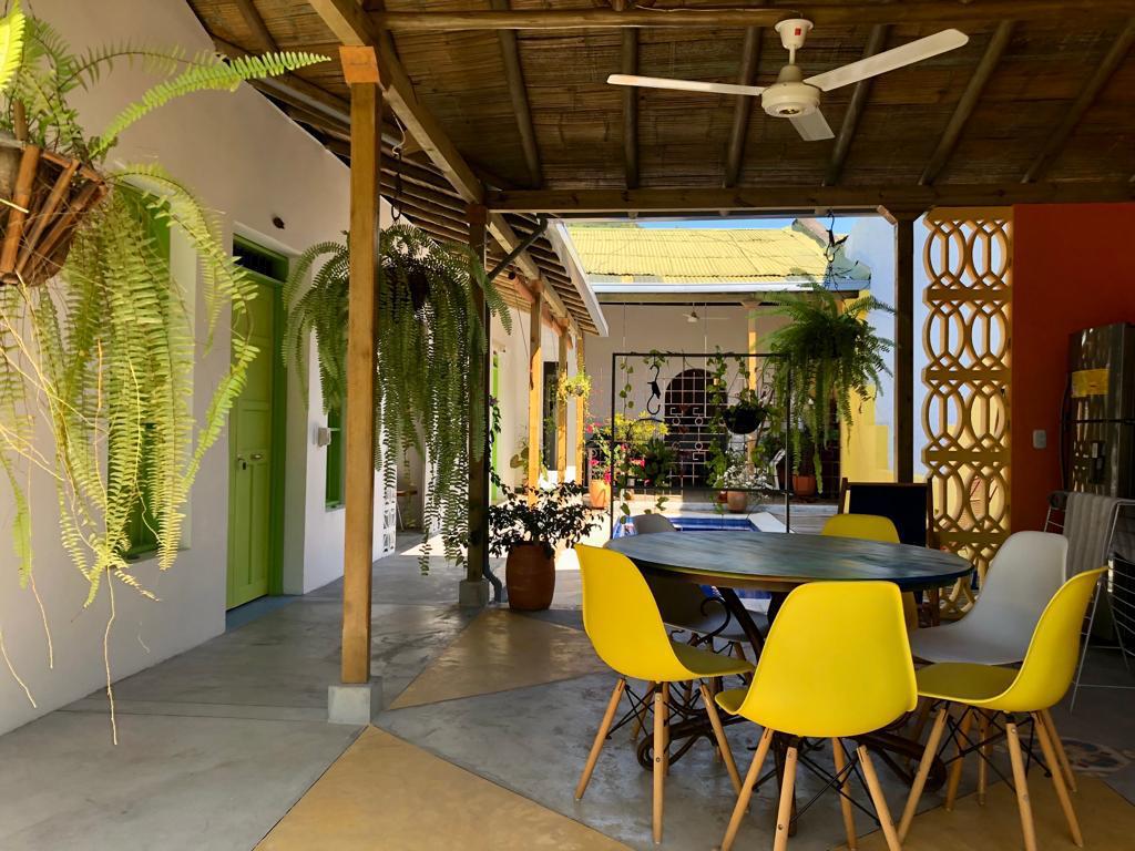 Tropical outdoor patio with yellow chairs, hanging fern plants, and a rustic bamboo roof.