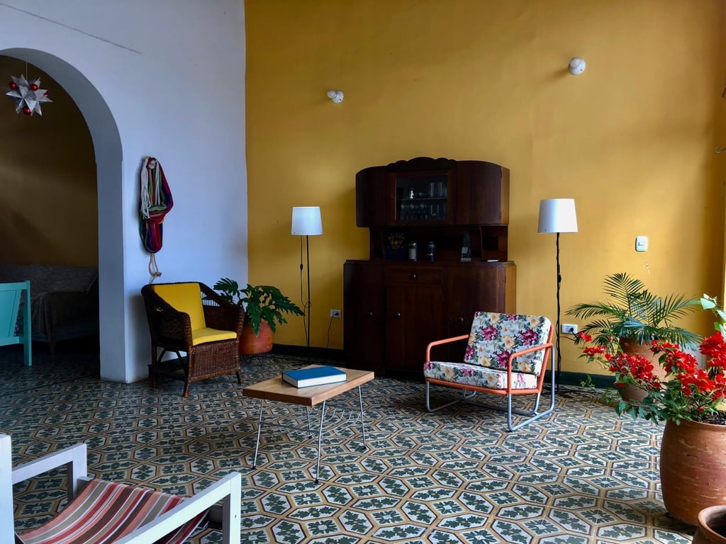 Eclectic living room with vintage furniture, yellow accent wall, and patterned tile flooring.