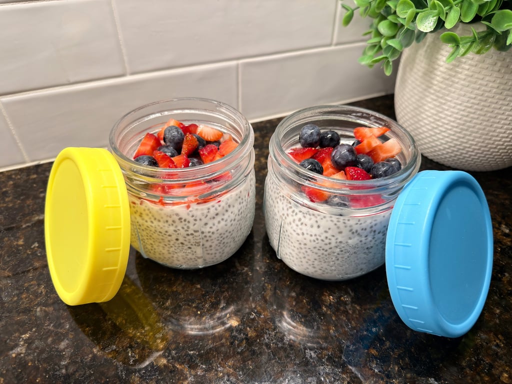 Two glass jars of chia pudding topped with fresh berries with colorful lids on a kitchen counter.