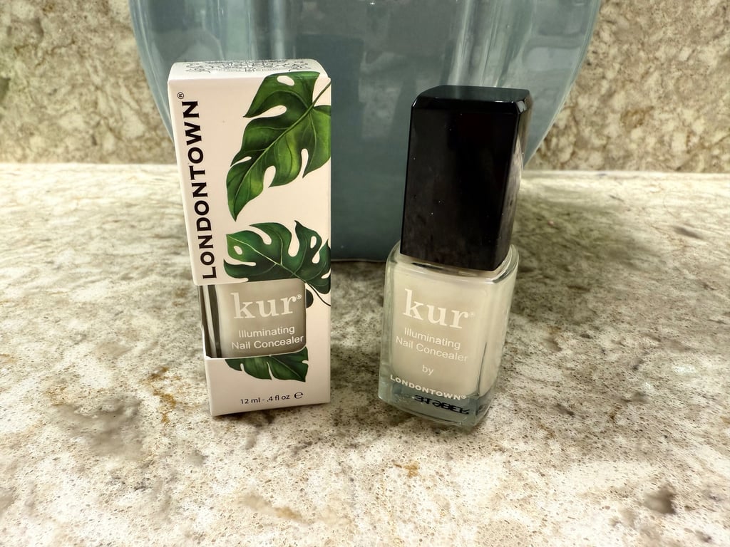 Londontown kur Illuminating Nail Concealer displayed with its box on a neutral countertop.