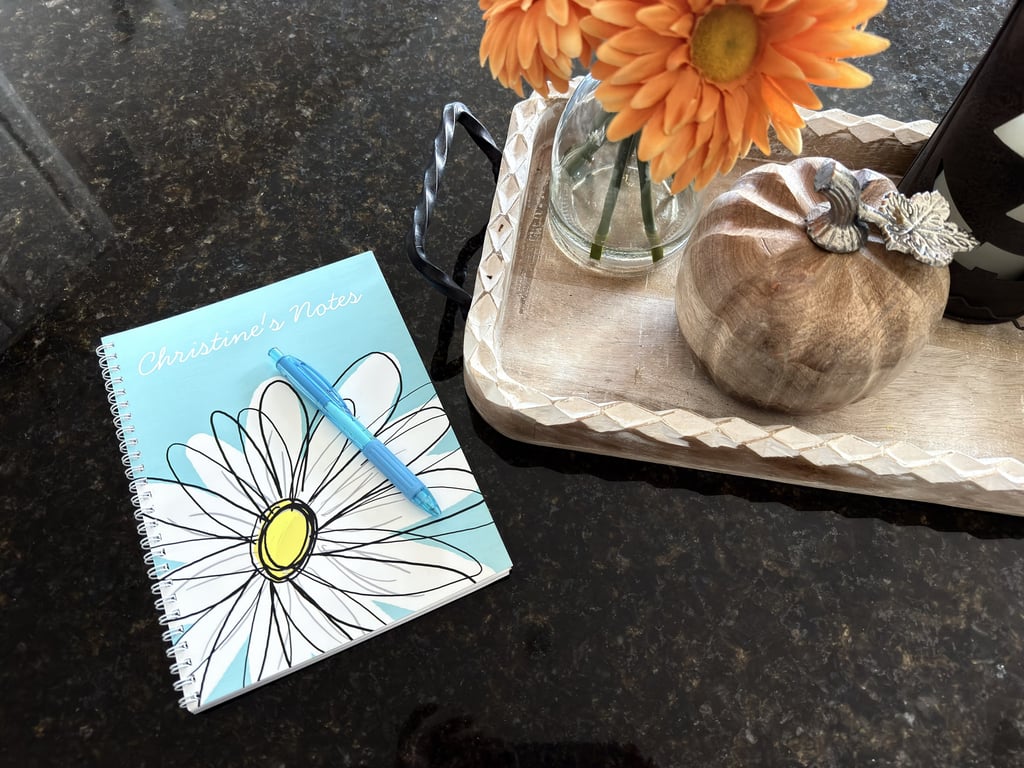Personalized notebook on a kitchen island with orange flowers and a small pumpkin as fall decor