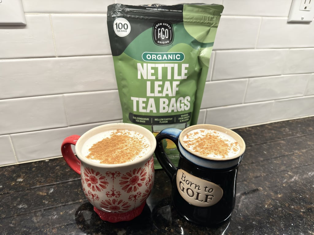 Two mugs of frothed nettle tea with cinnamon and a nettle tea bag on a kitchen counter