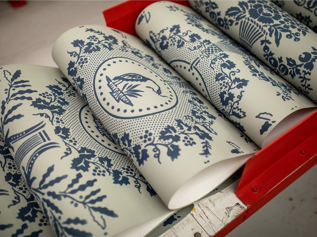 Rolls of vintage blue and white toile wallpaper with floral and bird patterns in a red rack.