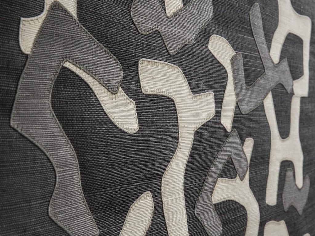 Close-up of grey and white textured fabric with abstract appliqué shapes for modern interior design.