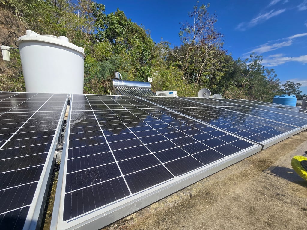 Photovoltaic solar panels installed on a rooftop with a water tank and solar heater under a clear blue sky.