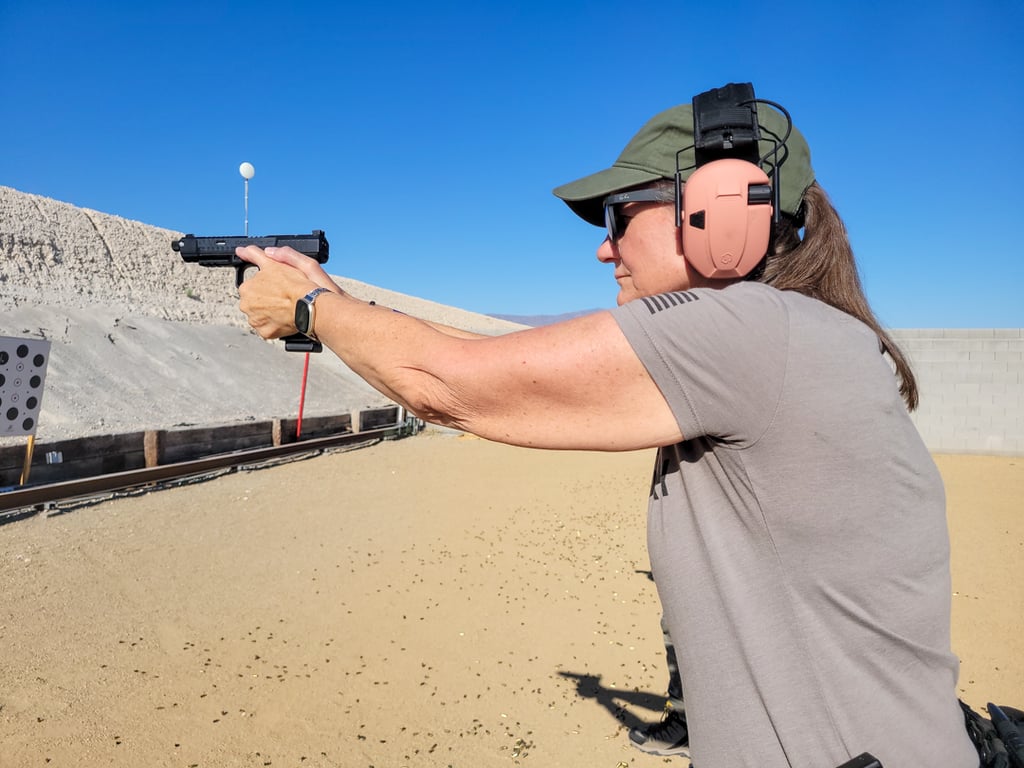 A woman at an outdoor firing range practicing target shooting with a black semi-automatic handgun.