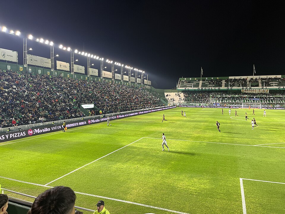 Estádio Florencio Sola cheio durante jogo em Buenos Aires, com torcida nas arquibancadas e campo iluminado à noite.