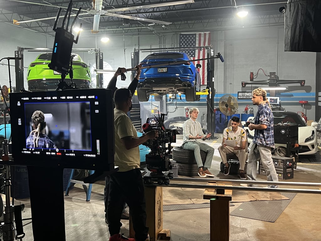 Professional film crew recording a video production in a car garage with exotic sports cars on lifts.