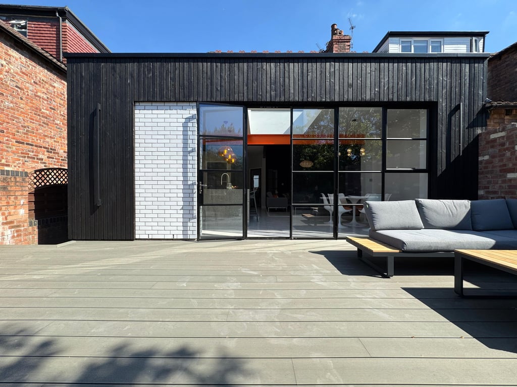Modern home extension with black timber cladding, sliding glass doors, and a spacious outdoor composite deck.