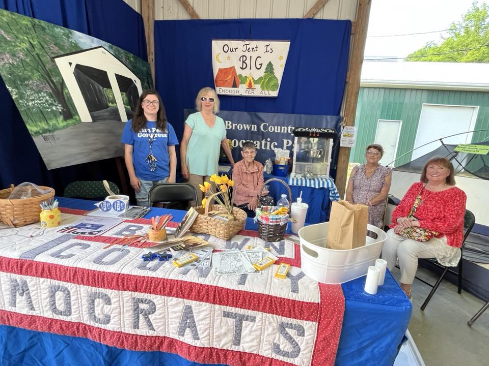 Five women sit or stand behind the Democrats booth at the fair