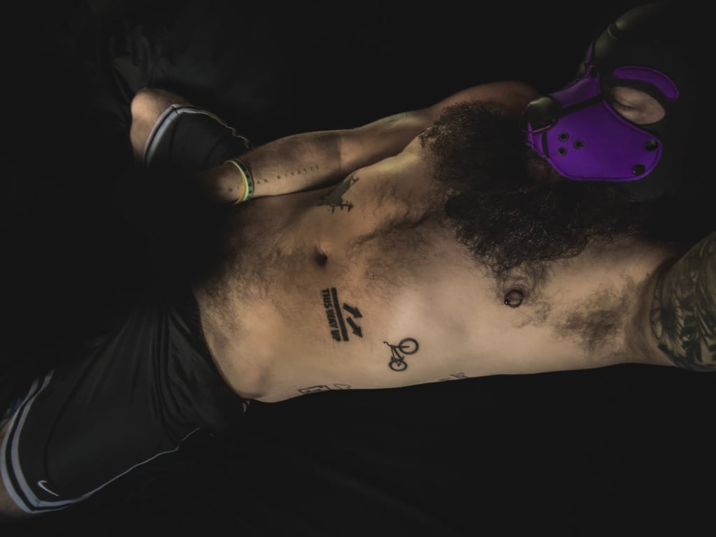 Shirtless man in pup mask, lying in bed in an intimate pose