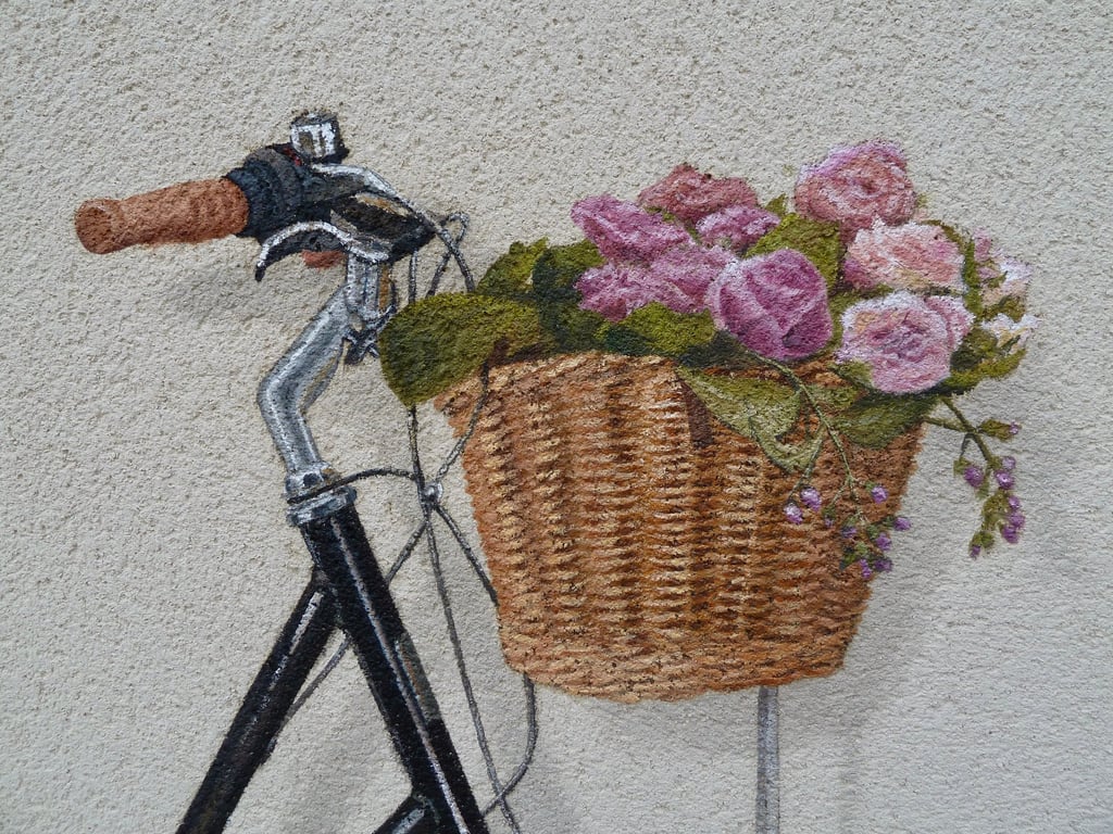 Détails d'un panier de vélo contenant des fleurs, peint en trompe-l'oeil sur une façade.