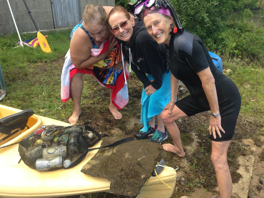 Susan Baur posed with two other women next to a kayak and a big of trash. All are in swimming gear. 