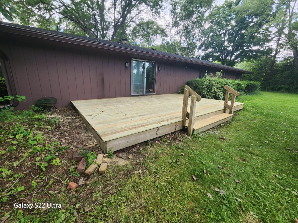 A newly installed wooden backyard deck with steps attached to a brown ranch-style house.