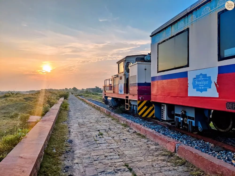 Heritage narrow-gauge train crossing Sambhar Lake at sunrise, bathed in golden light.