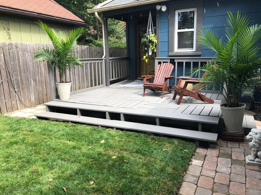 Backyard wooden deck with gray stain, Adirondack chairs, and potted palm trees.