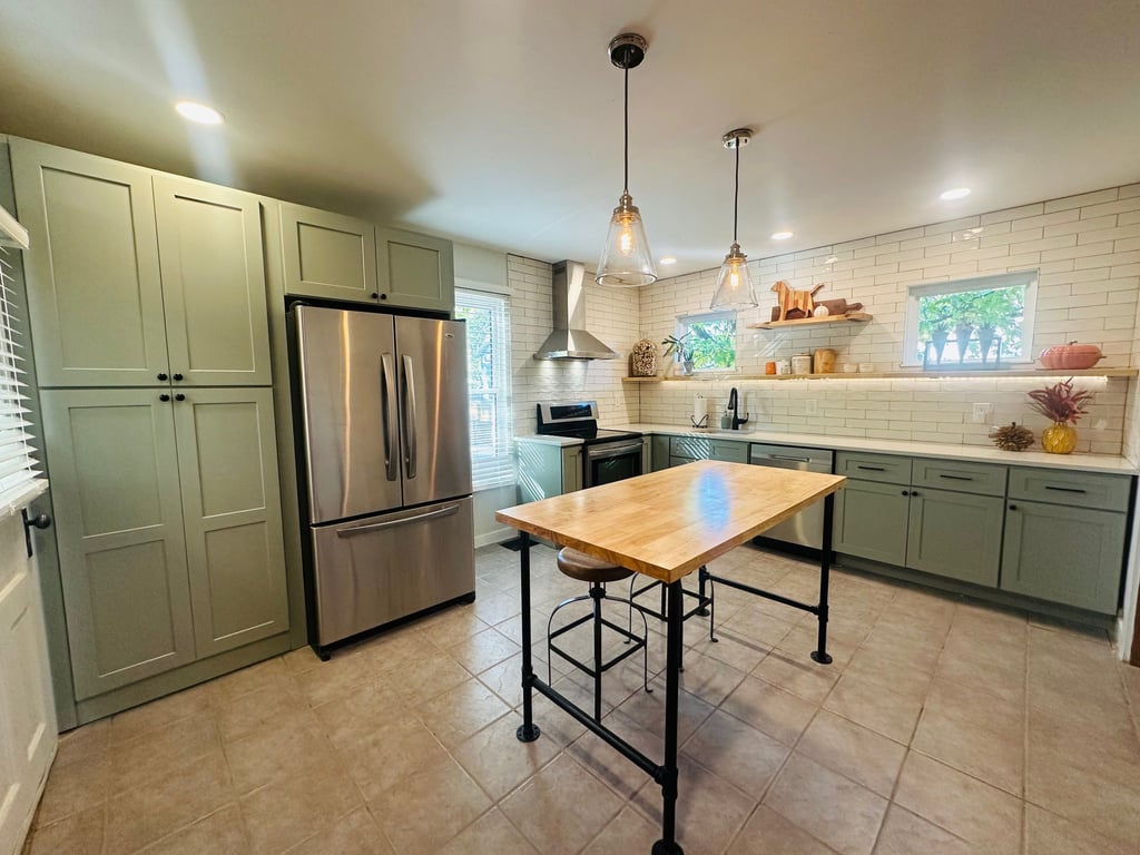 Modern kitchen with sage green cabinets, stainless steel refrigerator, and butcher block island.