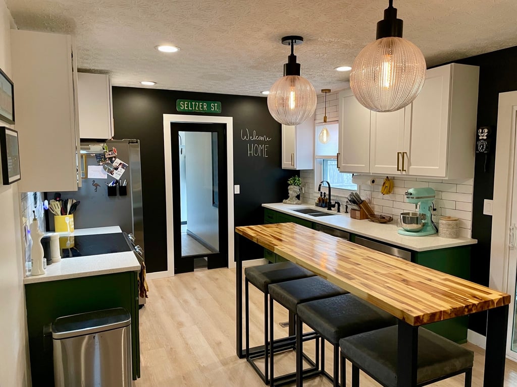 Modern kitchen with green cabinets, butcher block island, and globe pendant lighting.