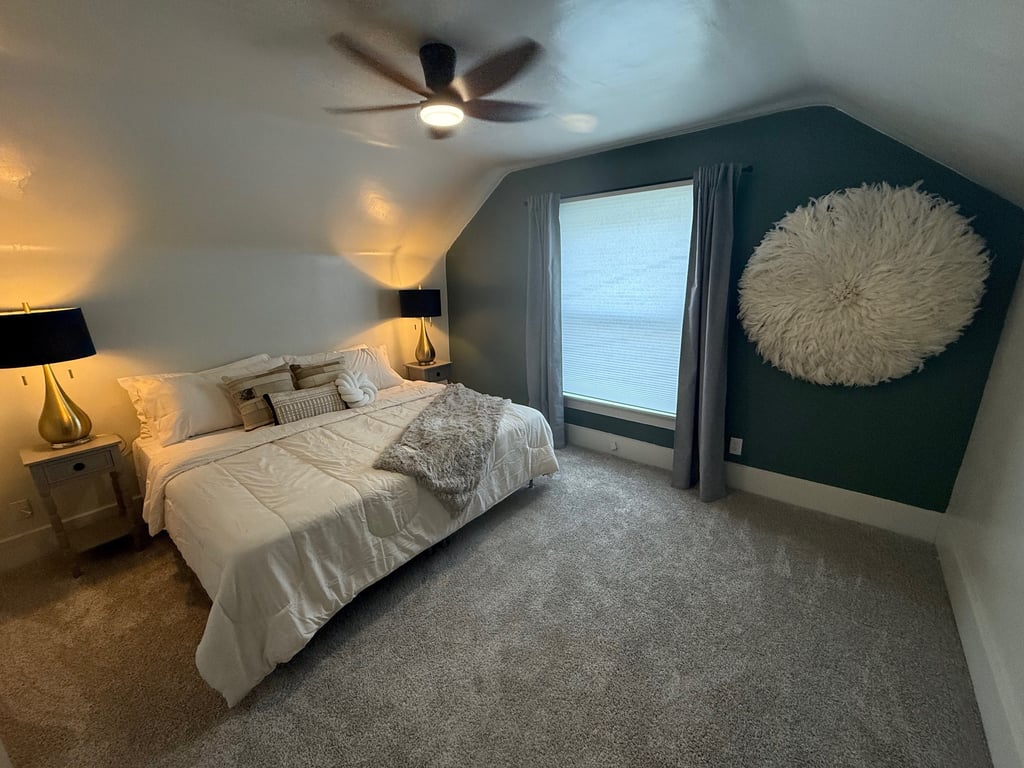Modern bedroom with a white duvet, dark green accent wall, and a large feathery wall decor.