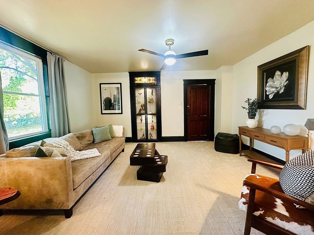 Modern living room with a tan leather sofa, dark wood coffee table, and an elegant lit display cabinet.