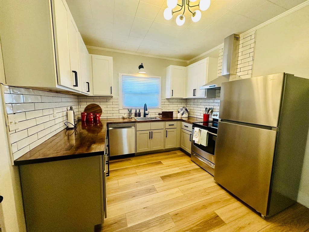 Modern kitchen with white upper cabinets, stainless steel appliances, and butcher block countertops.