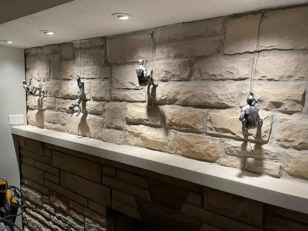 Miniature iron rock climber figurines hanging from a rustic stone wall mantel with accent lighting.