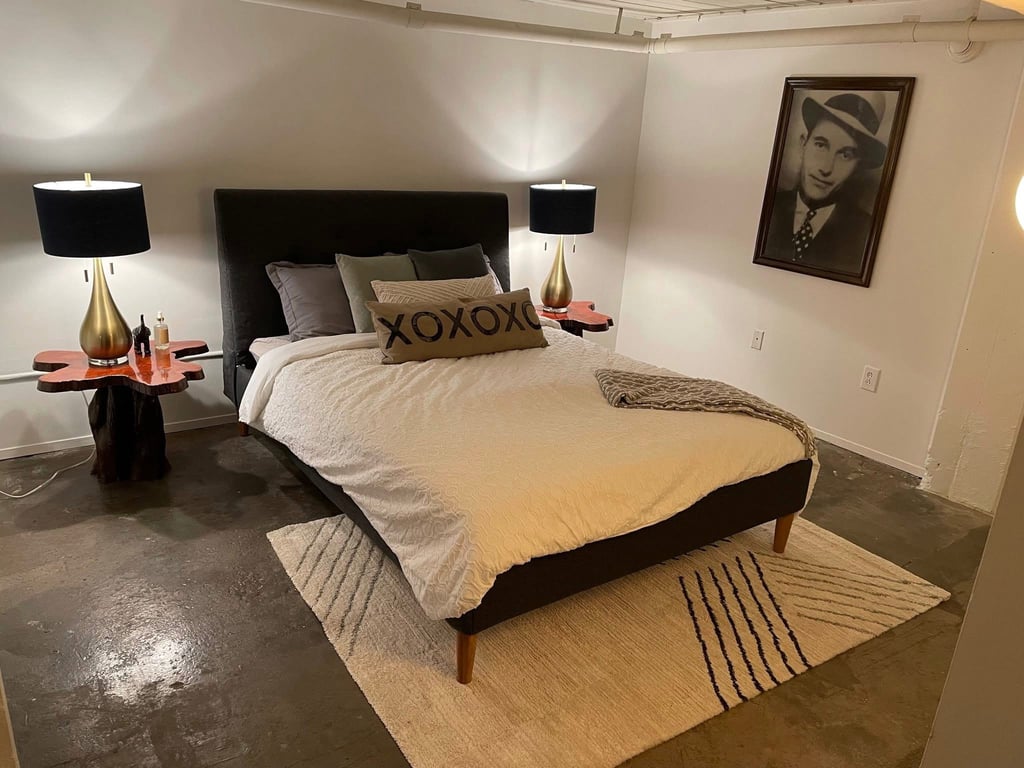 downtown loft bedroom with black upholstered bed, gold lamps, and live edge wood nightstands.