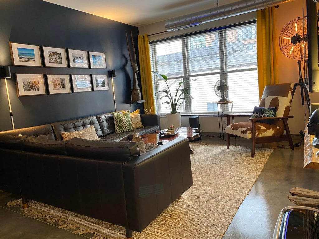 Modern industrial living room featuring a black leather sectional sofa, gallery wall, and cowhide chair.
