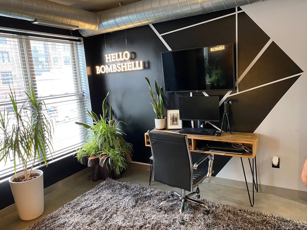 Ohio staged Modern home office with a wooden desk, black accent wall, neon sign, and indoor plants.