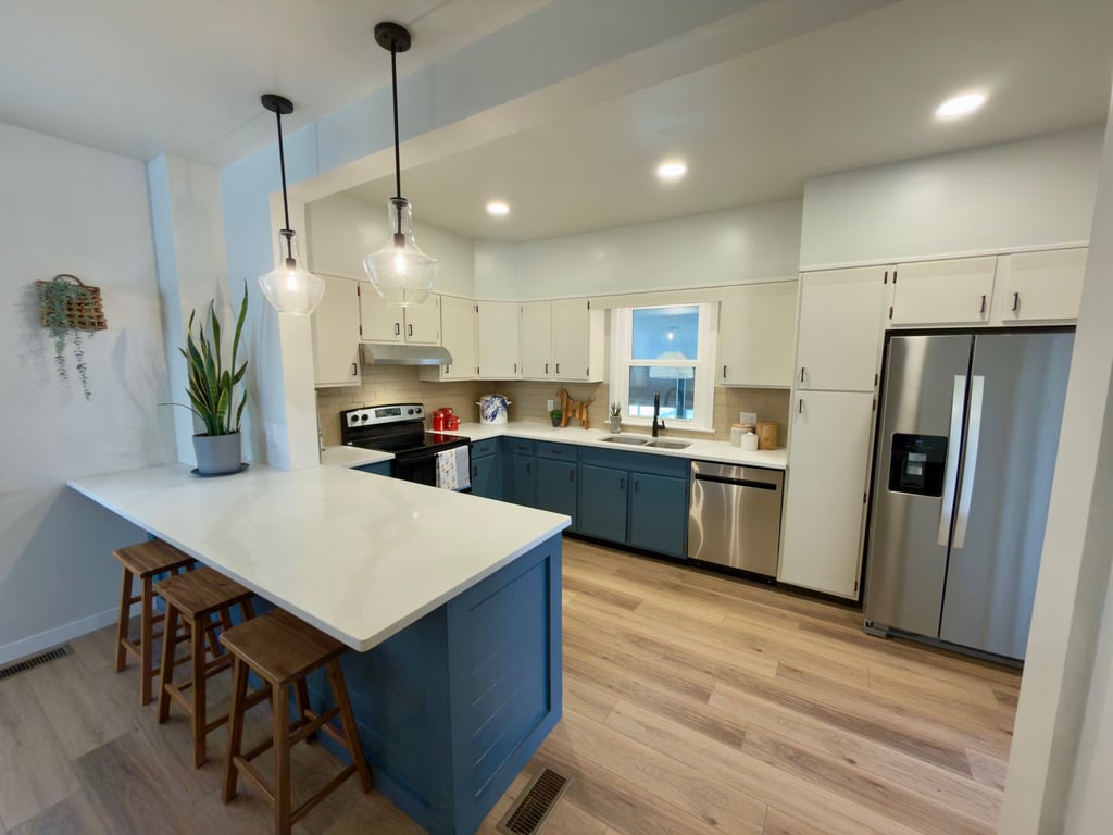 Modern kitchen with blue lower cabinets, white upper cabinets, a waterfall island, and stainless steel appliances.