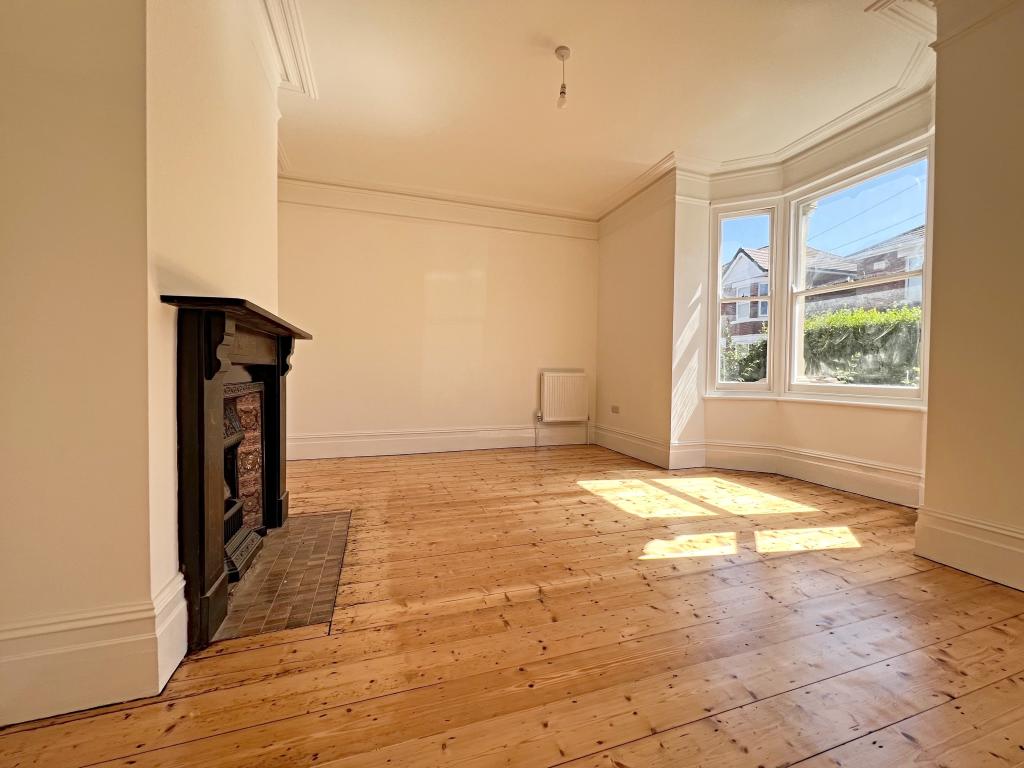 Spacious empty living room featuring original pine wood flooring, a vintage fireplace, and a bright bay window.
